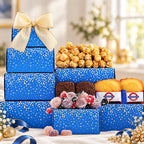 A gift assortment display featuring blue gift boxes with gold polka dots and a large cream bow, filled with caramel popcorn, chocolate brownies, macarons, and wrapped candies, set on a white tablecloth with festive gold ornaments.
