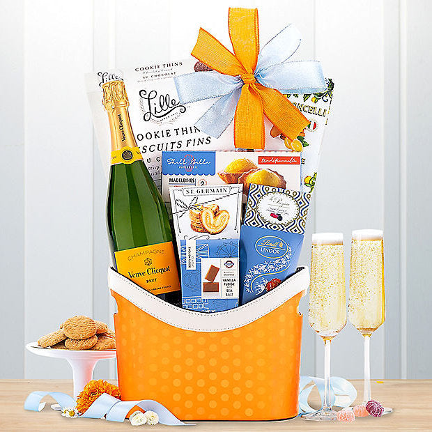 Gift basket with champagne, cookies, and snacks on a wooden table.