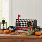 A personalized fall-themed mailbox styled on a wooden table with autumn props. The mailbox features a black and white buffalo check pattern on the lid, a red flag, a red base band with the white text 'THE BENJAMINS', and a circular 'Hello Fall' wreath decal.