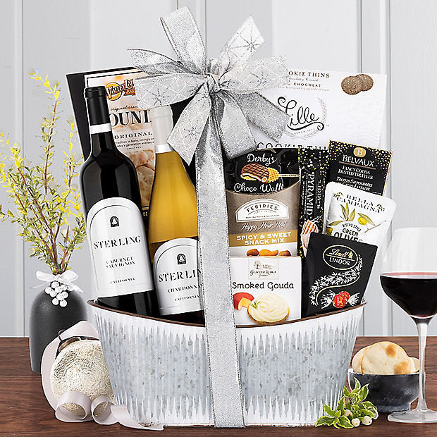 Gift basket with wine bottles, snacks, and a bow on a wooden table.
